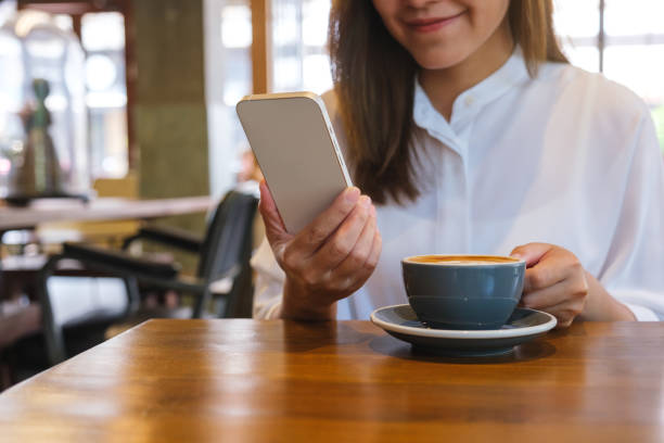 istock Closeup image of a young woman holding and using mobile phone while drinking coffee in cafe 1486058651