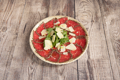 Marbled dish with typical Italian beef carpaccio with arugula and parmesan cheese flakes on gray table