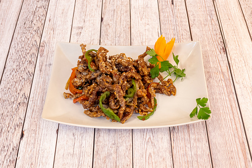 Chinese recipe of fried caramelized beef strips with fried red and green peppers and sesame seeds with onion on a white plate