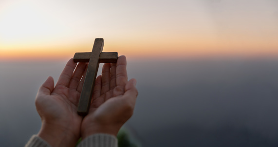 Person hands palm up praying and worship of cross with Belief in Jesus Christ. Eucharist therapy god blesses help, hope, and faith, Christian religion concept on sunset background.