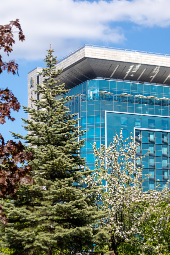 Modern, blue glass hotel building facade in spring greenery on Freedom square in Kharkiv city, Ukraine. Travel recreation architecture