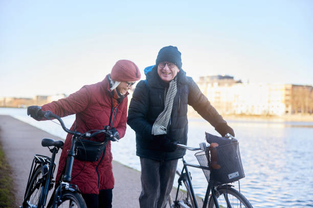 istock Laughing senior couple talking while walking with bicycles by a river in winter 1486067468