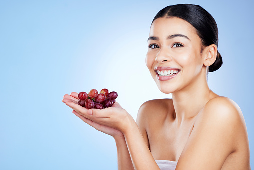 Grape, woman and portrait for face skincare, cosmetics or food product on studio background. Happy young model, grapeseed fruit and oil of nutrition, vegan diet or detox wellness of natural aesthetic