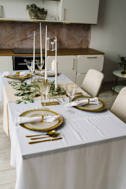 istock Festive table setting with plate, golden cutlery set and eucalyptus leaves, candles. Dinner table decorated for cozy fall holiday gathering in kitchen. Modern panel kitchen interior with countertop. 1486070220