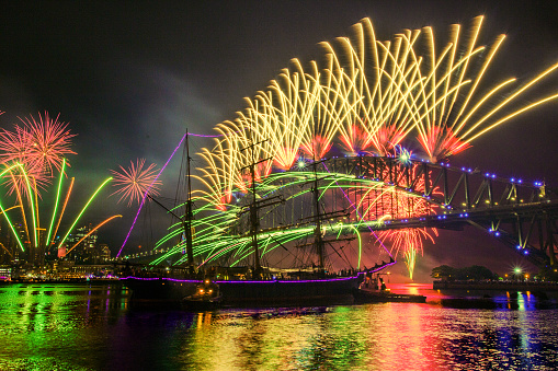 The scene of the New Year's Eve Firework celebration in Sydney Harbour Bridge with a classic sailboat on the river