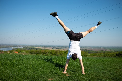 young guy standing on his hands, training in nature, beautiful landscape, mental and physical health