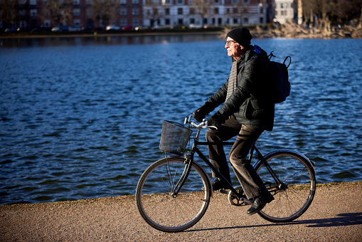 Senior man riding on his bicycle along a footpath by a river on a sunny day in winter