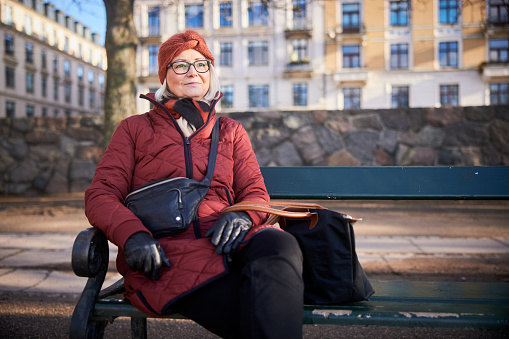 Senior woman wearing a scarf and jacket smiling while sitting on a park bench in the wintertime