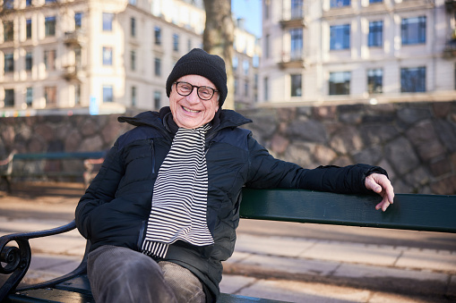 Portrait of a smiling senior man in a scarf and jacket sitting on a park bench in the wintertime