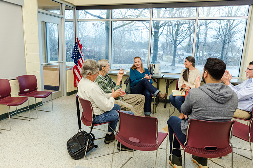 The diverse group of retired military veterans clap and smile when meet for their support group in a room at the community center.