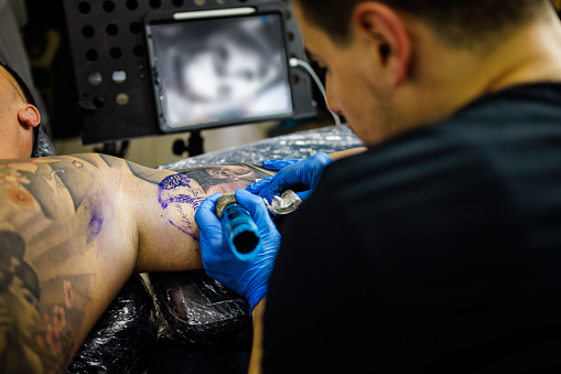 Two men, tattoo artist tattooing a man's arm in his tattoo studio.