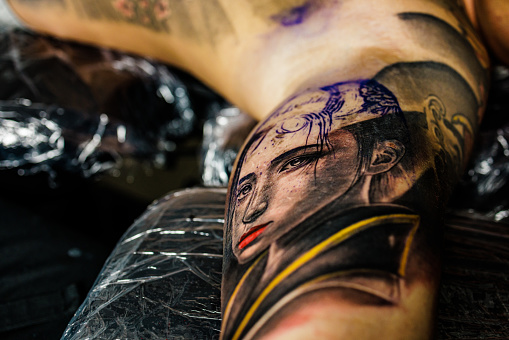 Two men, tattoo artist tattooing a man's arm in his tattoo studio.