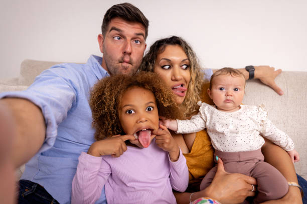 Point of view shot of a phone's perspective of a father taking a selfie with his family. The mother and oldest daughter are pulling funny faces.