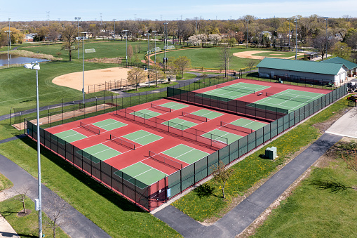 Aerial view of a pickleball facility with red and green courts in a suburban park with baseball and softball fields in early spring.