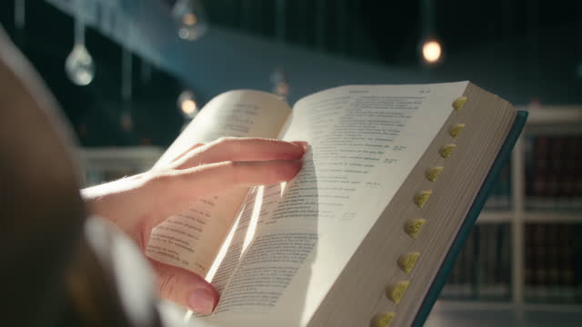 Female hands hold an open book Holy Bible in university library. Warm light illuminates pages. Theologian studies the history of the World. Reading learning education concept.