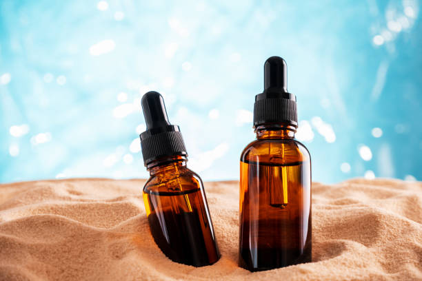 bouteilles en verre brun avec des huiles cosmétiques sur une plage de sable. concept de soins de la peau d’été. - sandy brown photos photos et images de collection