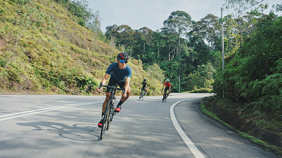 Young professional athlete riding bicycle for exercise on the road through the countryside. He is well equipped, with protective helmet, sunglasses, black and red jersey. Photo taken when cyclist is in motion, from car in motion, for speed effect.