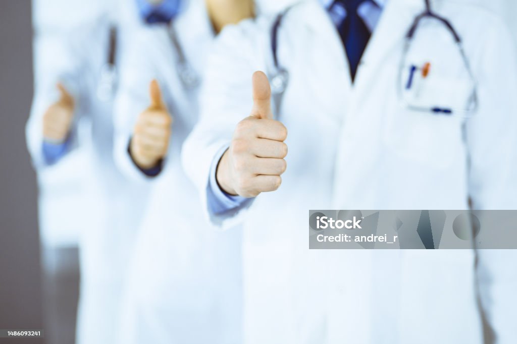 Group of unknown doctors stand as a team with thumbs up in a hospital office. Physicians ready to examine and help patients. Medical help, insurance in health care, best desease treatment and medicine concept Group of unknown doctors stand as a team with thumbs up in a hospital office. Physicians ready to examine and help patients. Medical help, insurance in health care, and medicine concept. A Helping Hand Stock Photo