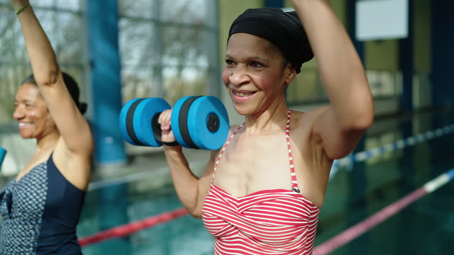 Happy senior woman exercising with foam dumbbells in fitness class