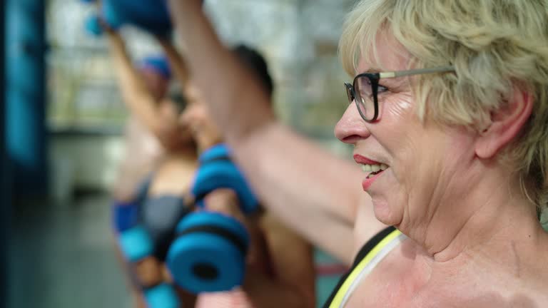 Senior woman exercising with foam dumbbells in fitness class