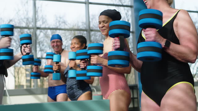 Seniors fitness class exercising with foam dumbbells by a swimming pool