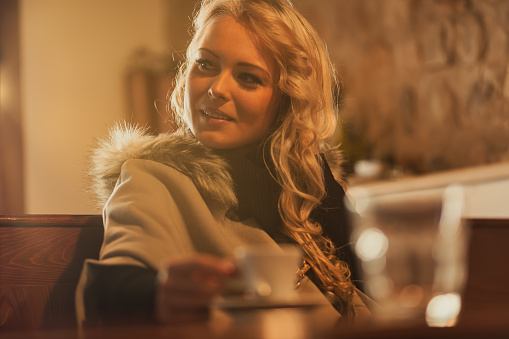 In sunlit European haven, young wanderer sips espresso's soul. Winter's chill forgotten; wrapped in fur, beauty radiant. Solitude embraced, yet open to serendipity