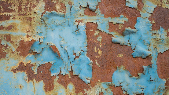 An old pitted and weathered rusty metal sheet background framed by old rusty bolts. Lots of texture with subtle abstract colors of the patina.