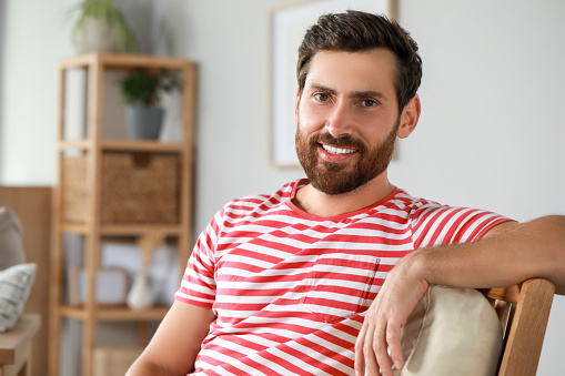 Portrait of handsome bearded man in armchair at home, space for text