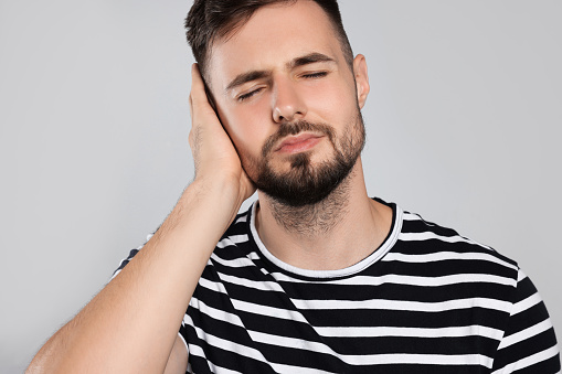 Young man suffering from ear pain on light grey background