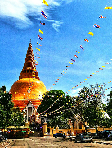 Nakhonpathom, Thailand-April 18, 2018: Beautiful golden pagoda with Thai flag and blue sky background. Religion, Ancient exterior design and Landmark for travel in Nakhon Pathom province, Thailand.