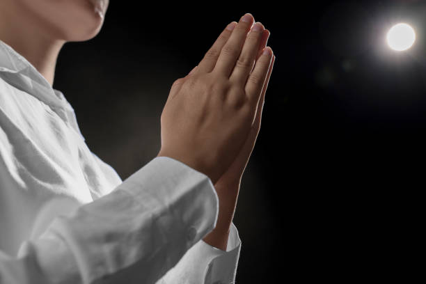 istock Woman holding hands clasped while praying on black background, closeup 1486113561
