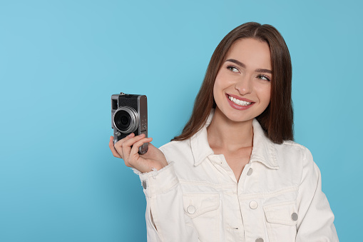 Young woman with camera on light blue background, space for text. Interesting hobby