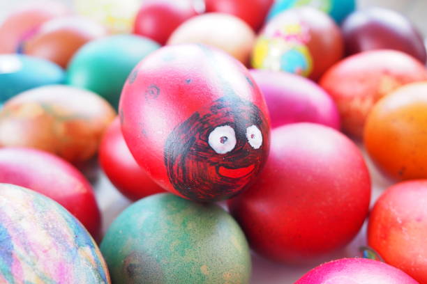Easter egg - ladybug. An egg painted red and black with a cheerful face. Easter colorful eggs. Boiled chicken dyed eggs with red, pink, blue, green, yellow, orange and brown shells. Fun background.