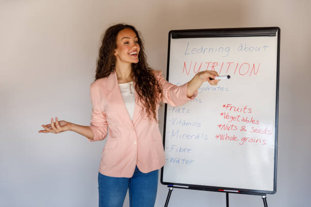 istock Professional female nutritionist standing by a whiteboard, holding a presentation on basics of nutrition 1486114111