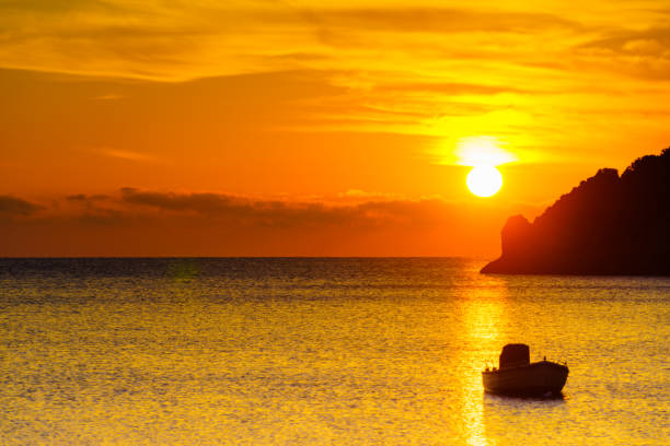 Scenic sunrise or sunset over sea surface, boat anchored in bay, Greece