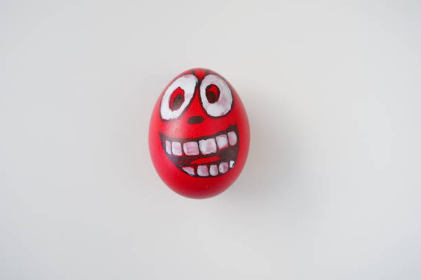Easter egg painted red, white and black with a cheerful toothy face. Boiled chicken dyed egg with red shell. White background. Big eyes, white teeth on the fun face. Copy space.