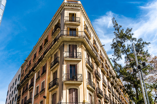 Apartment complex in Barcelona, Spain. Beautiful art nouveau building, with its striking facade and surrounding residential neighborhood. The bright blue sky highlights the majestic tower against the clouds.