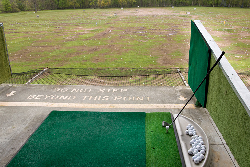 Golf driving range with golf mat and golf balls on second level. Warning sign, “Do not step beyond this point”.