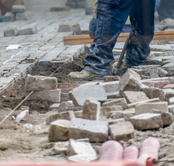 worker laying interlocking pavers during sidewalk construction with raised soil full of pipes and pipes to be laid. - subcontractor imagens e fotografias de stock