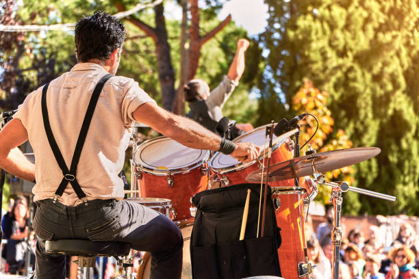 Summer music festival at the park. Music band jumping while performing on the stage. Drummer plays while singer puts his fist up in a success expression. Street art public performance in Madrid performance group stock pictures, royalty-free photos & images