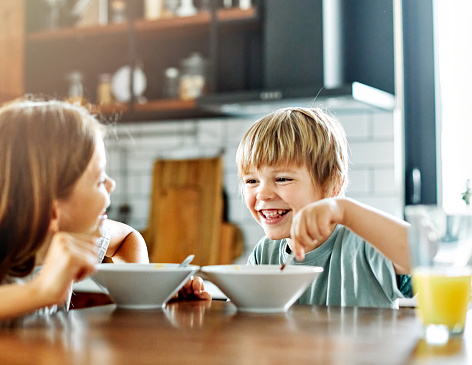 Portrait of brother and sister having fun together eating breakfast strawberries in kitchen