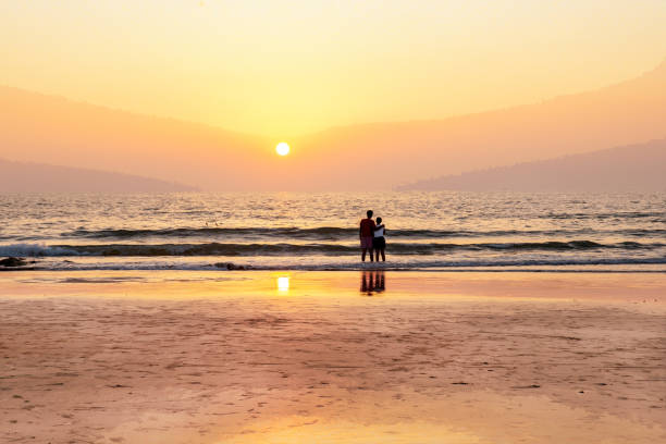 Idyllic  pink view in Goa  (Kerala  or Karnataka) Couple (relationship)  and orange sunset on Indian ocean   (unrecognizable persons from back)