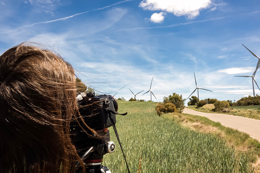 Rear view of photographer shooting wind turbines in a green wheat field