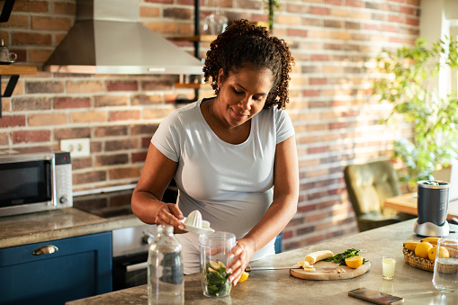 Close up of a Young Pregnant Woman preparing a healthy smoothie in the kitchen