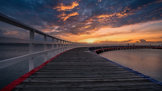 A scenic view of a long pier illuminated by the warm orange hues of the sun in Geelong, Victoria, Australia