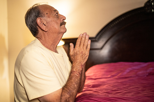 Senior man praying in the bedroom at home
