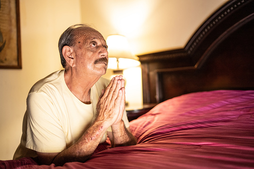 Senior man praying in the bedroom at home