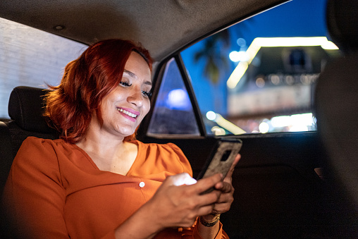 Mid adult woman using mobile phone during a taxi drive