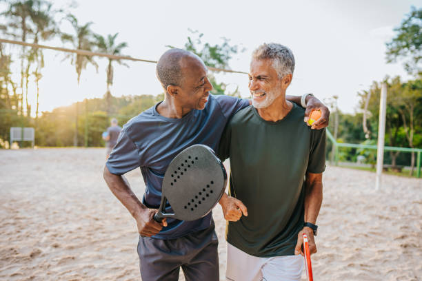 два старших друга играют в пляжный теннис - senior adult outdoors wellbeing sky стоковые фото и изображения