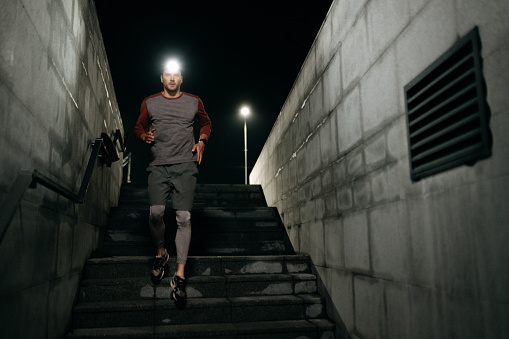 Handsome athlete man with headlamp running on stairs during night time